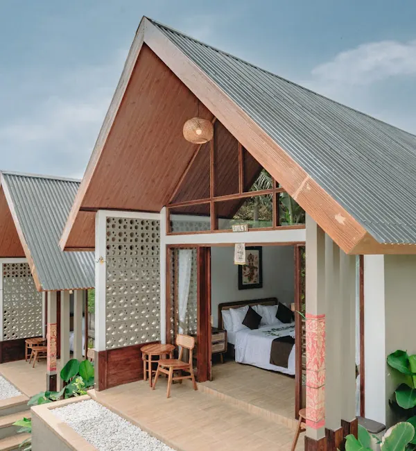 An A-frame cottage with its glass doors open to a made bed, rattan chairs on the terrace