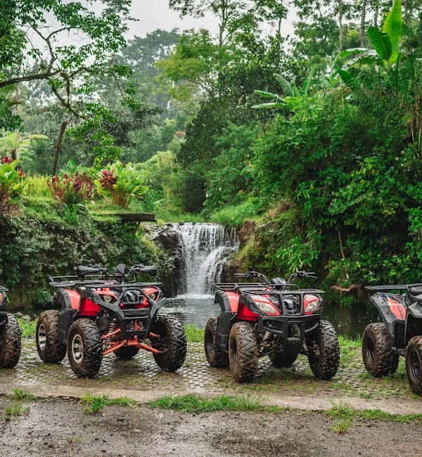 Red ATV quad bikes parked beside a jungle waterfall