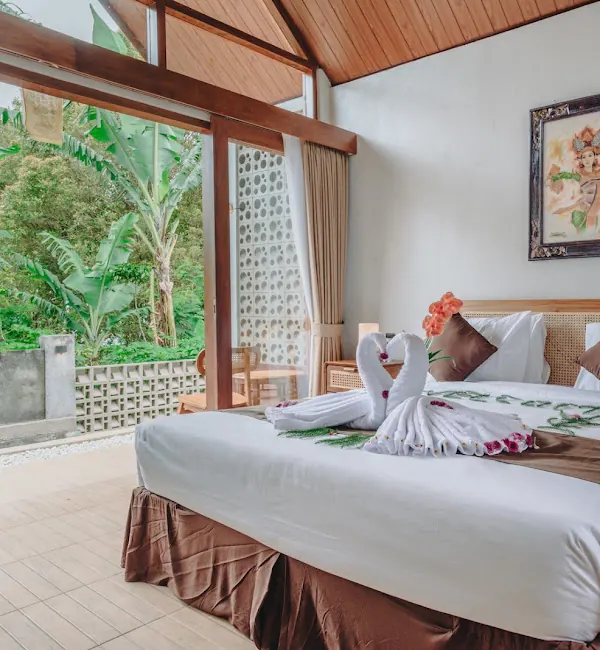 Double room with a rattan headboard, white linen and glass doors looking out to banana trees